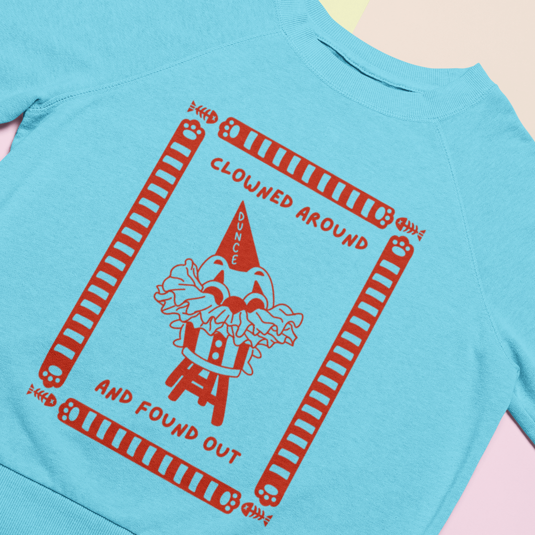 Light blue t-shirt with red clown graphic and text on a light pink background.